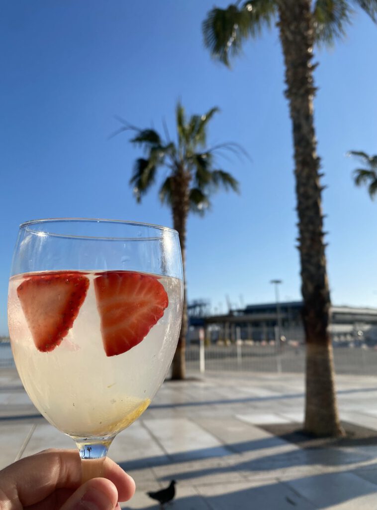 Glas met koude drank en aardbeien bij de haven van Málaga, met palmbomen en blauwe lucht