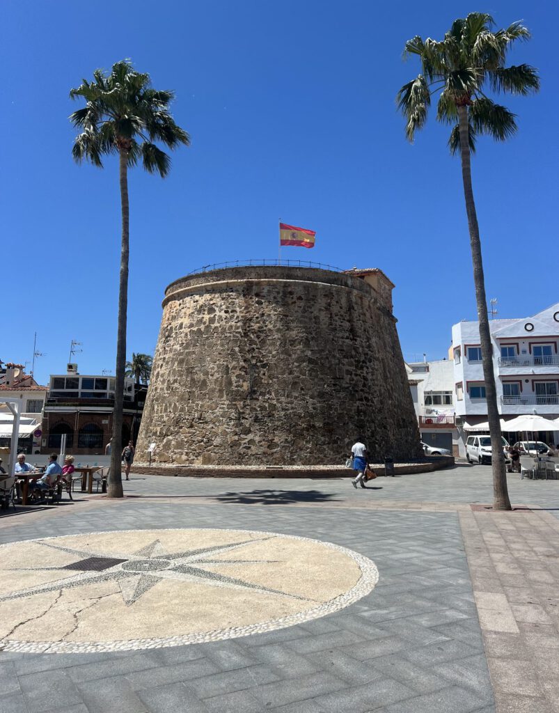 Oude ronde wachttoren met Spaanse vlag op een plein met palmbomen aan de Costa del Sol